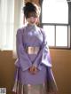 A woman in a purple kimono standing in front of a window.