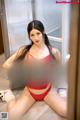 A woman in a red lingerie sitting on the floor.