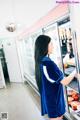 A woman in a blue dress standing in front of a refrigerator.