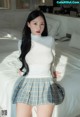 A woman in a white top and plaid skirt posing on a bed.