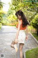 A woman in a white skirt and orange top is walking down a path.