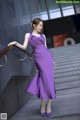 A woman in a purple dress is standing on some steps.