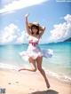 A woman in a white dress and hat jumping on the beach.