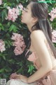 A woman sitting in front of a bush of pink flowers.