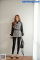 A woman standing in front of a white wall holding a black bag.