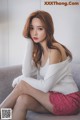 A woman sitting on a couch wearing a white sweater and pink skirt.