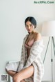 A woman in a pink bra and a white robe sitting on a bed.