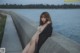 A naked woman sitting on a concrete wall by the water.