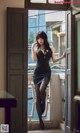 A woman in a black dress standing by a window.