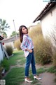 A woman standing in front of a house wearing a plaid shirt and jeans.