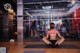 A woman in a pink top and black shorts sitting on a yoga mat.