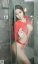 A woman in a red bodysuit standing in a shower.