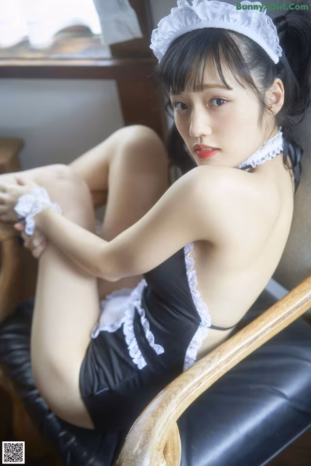 A woman in a maid outfit sitting on a chair.