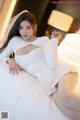 A woman in a white dress sitting on a bed.