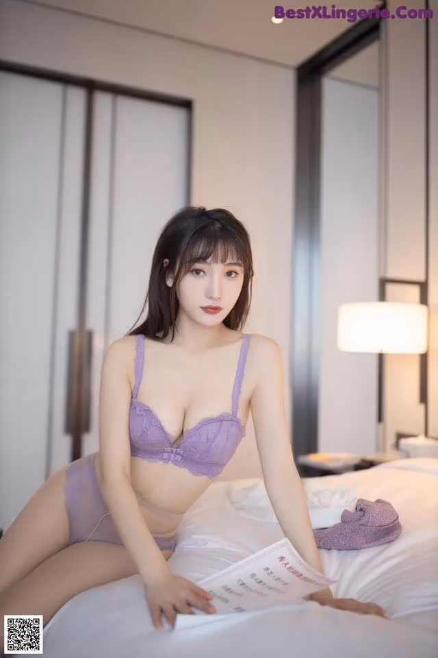 A woman in a purple lingerie sitting on a bed.