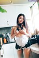 A woman in a maid outfit posing in a kitchen.