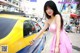 A woman in a pink dress standing next to a yellow car.