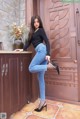 A woman in a black top and blue jeans leaning against a wooden door.