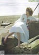 A woman in a white dress sitting on a rock by the ocean.