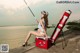 A woman sitting on top of a cooler holding a fishing rod.