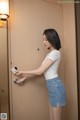 A woman in a white shirt and denim skirt opening a door.