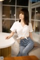 A woman sitting at a table in a white shirt and jeans.