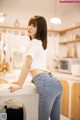 A woman in a white shirt and blue jeans leaning on a counter.