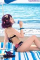 A woman in a bikini sitting on a beach next to the ocean.