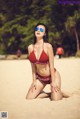 A woman in a red bikini sitting on a sandy beach.