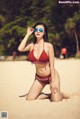 A woman in a red bikini sitting on a beach.