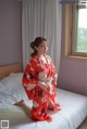 A woman in a red kimono sitting on a bed.