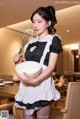 A woman in a maid outfit holding a bowl and a whisk.